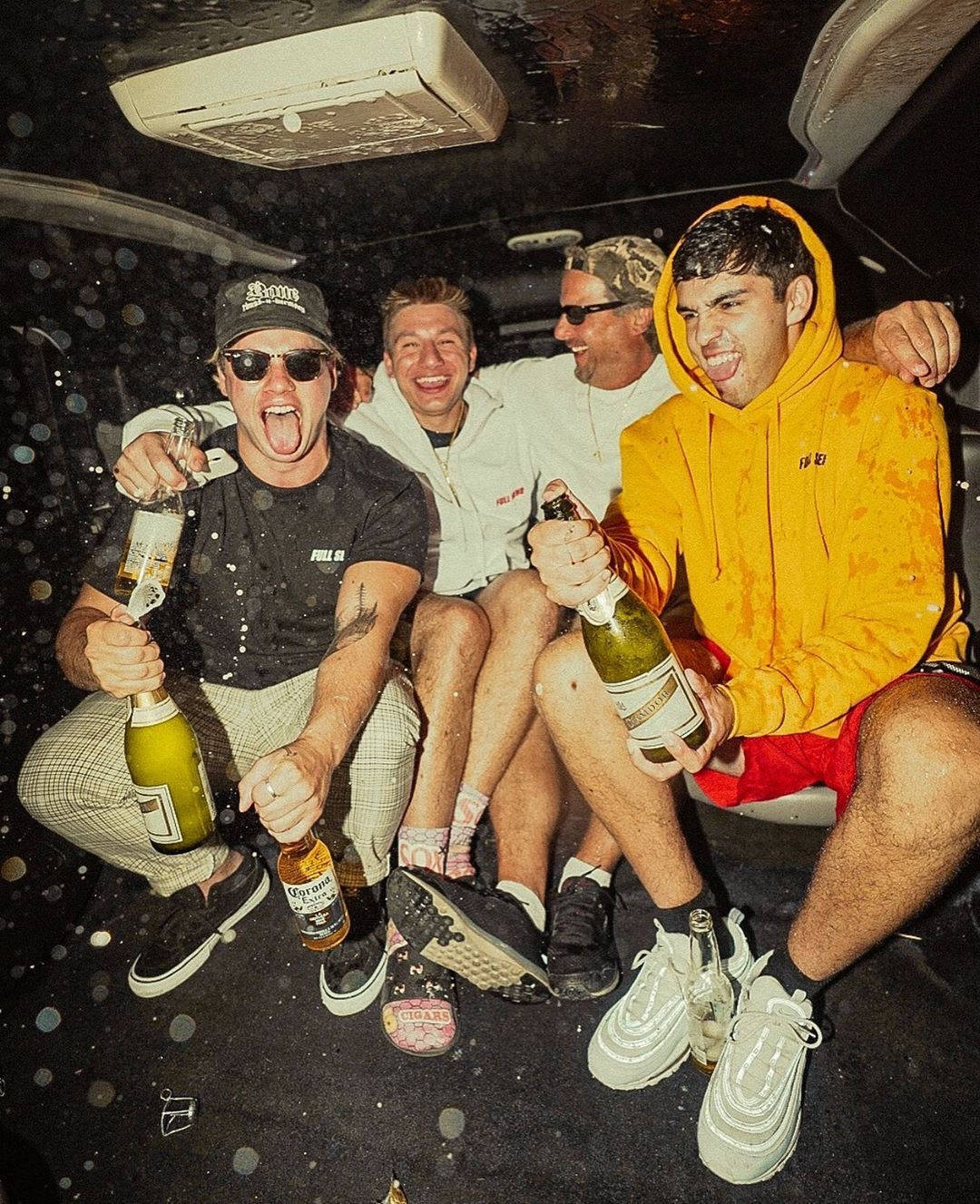 Four Men Sitting In The Back Of A Car With Bottles Of Champagne Background