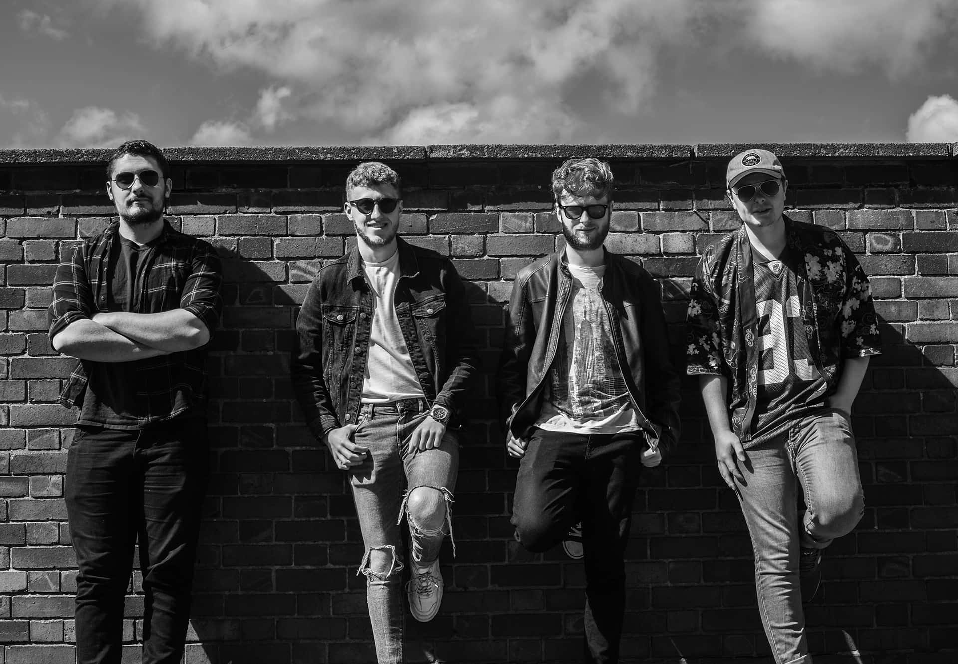 Four Young Men Standing In Front Of A Brick Wall