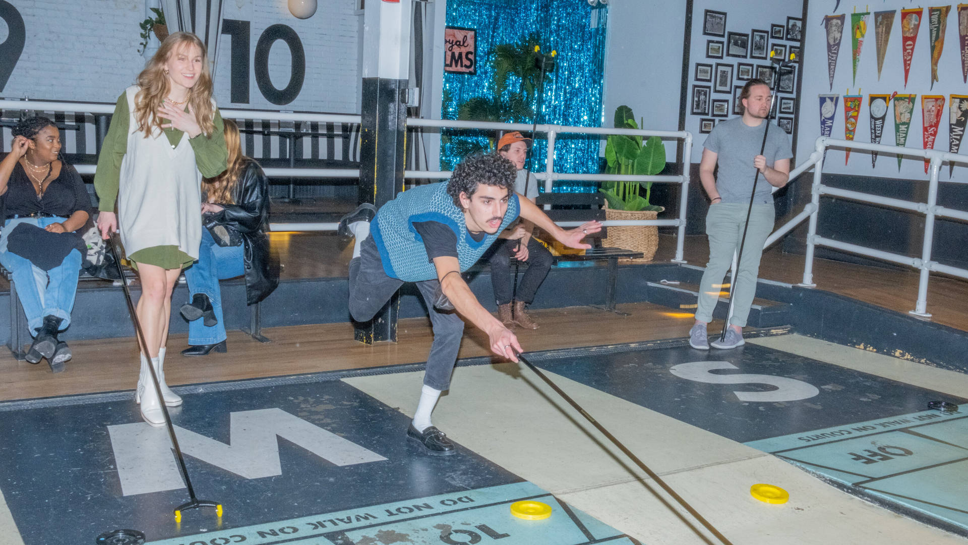 Friends Playing Royal Palms Shuffleboard Club In Brooklyn Background