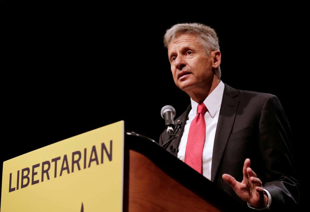 Gary Johnson Wearing Black Suit On A Podium Background