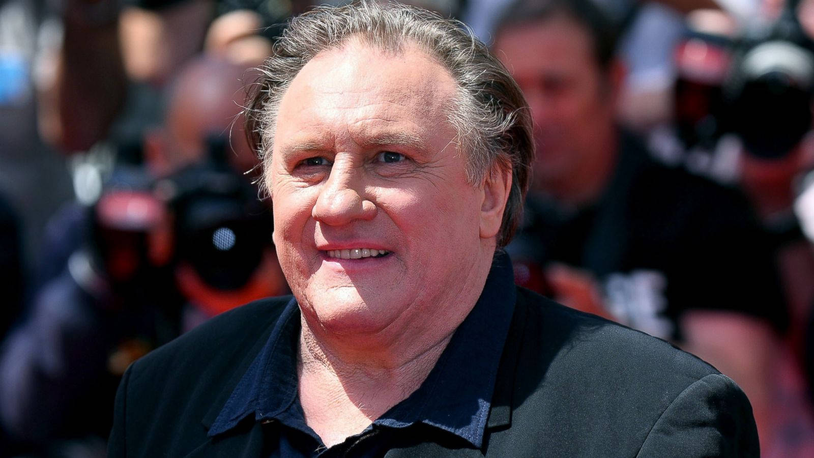 Gérard Depardieu Smiling With Press Background