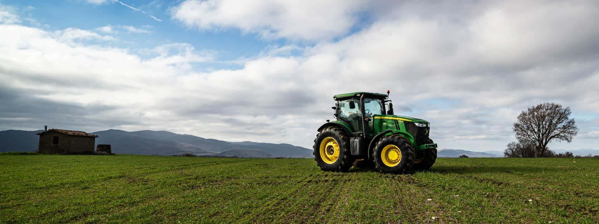 Green_ Tractor_in_ Field_with_ Mountain_ Backdrop Background