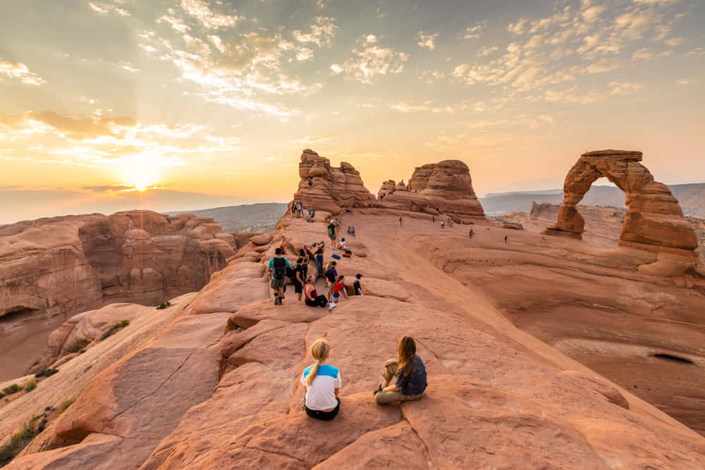 Group Travelers At Delicate Arch Background