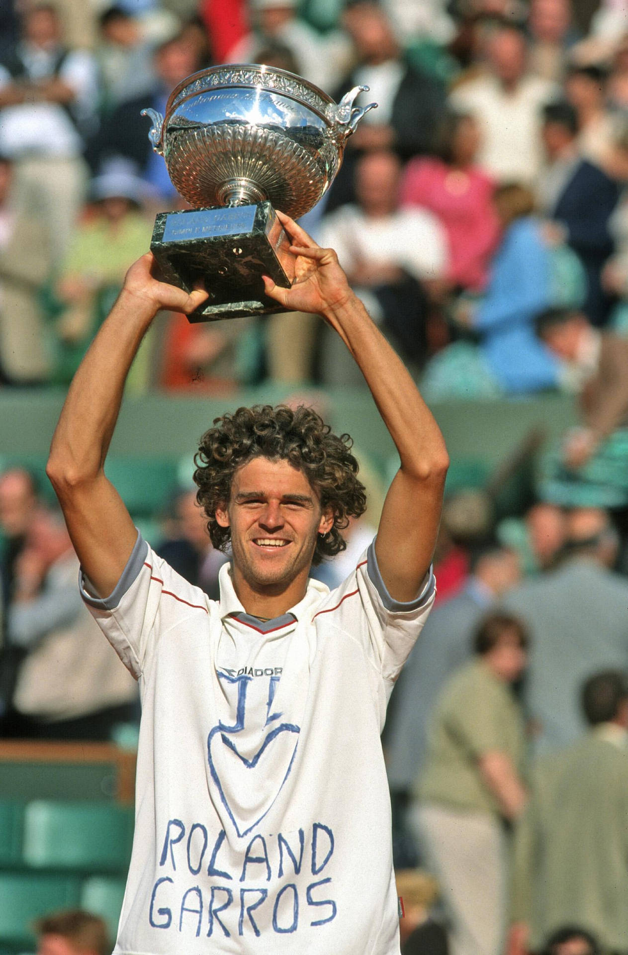 Gustavo Kuerten Jubilantly Lifting A Trophy After A Match Victory. Background