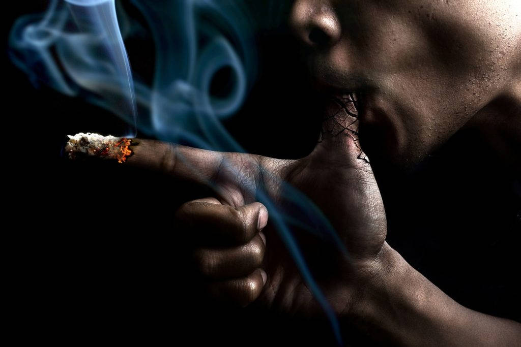 Hand Holding A Smoldering Cigarette Against A Dark Background Background