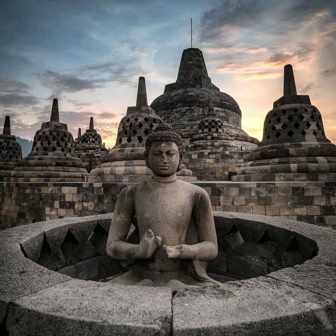 Harmonious Serenity: A Statue Of Buddha Overlooking The Magnificent Borobudur Temple Background