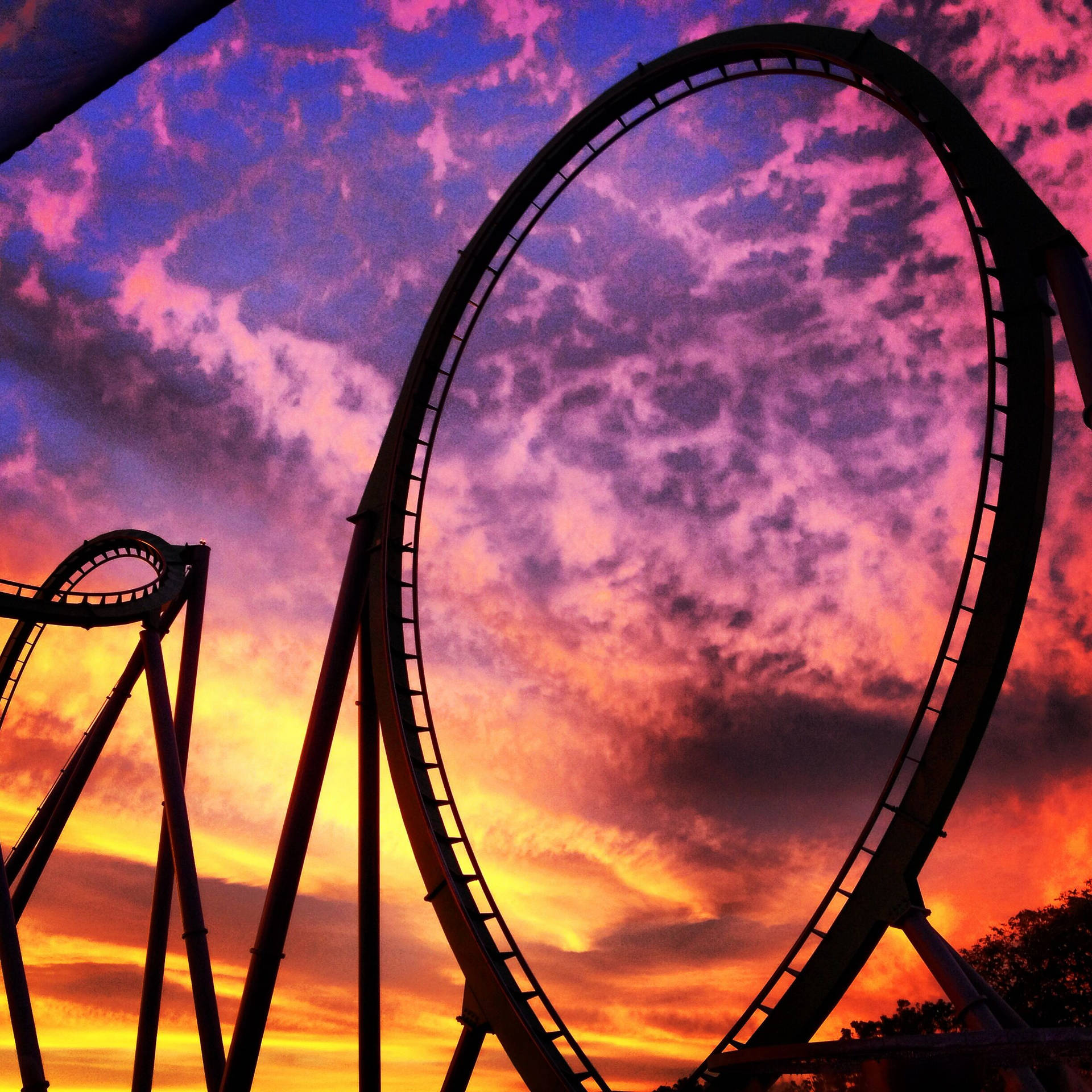 High-flying Thrill On A Roller Coaster Amidst Vibrant Sunset Background