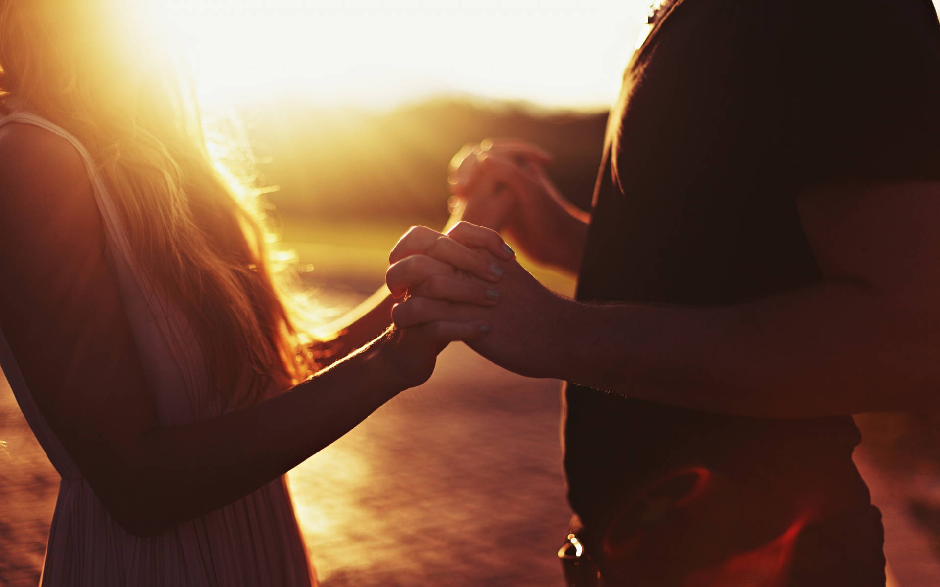 Holding Hands While Facing Each Other At Sunset Background