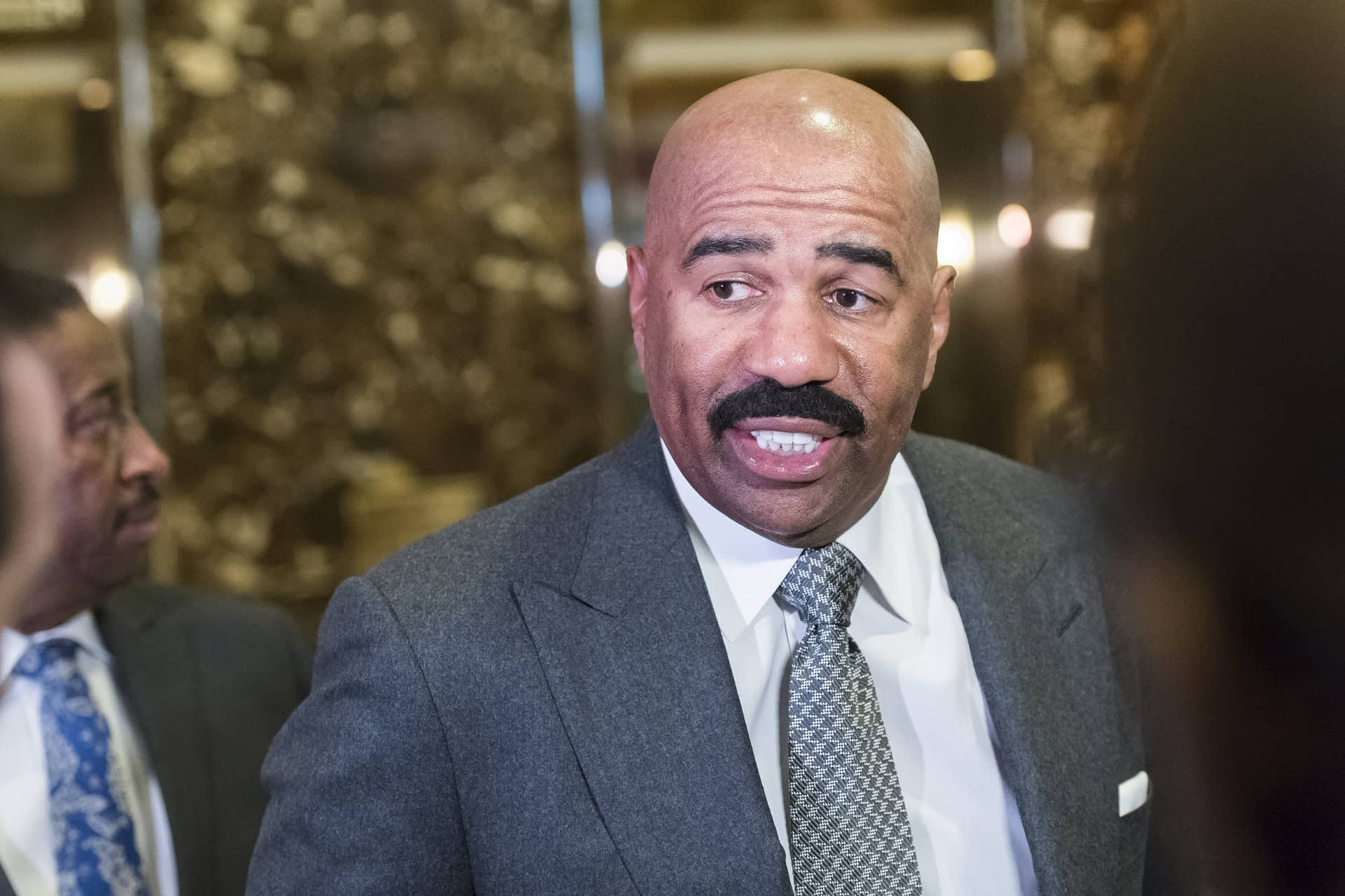 Iconic American Tv Host: Steve Harvey In Gray Suit Background