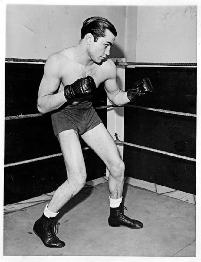 Image Barney Ross Standing Tall With A Gun Background