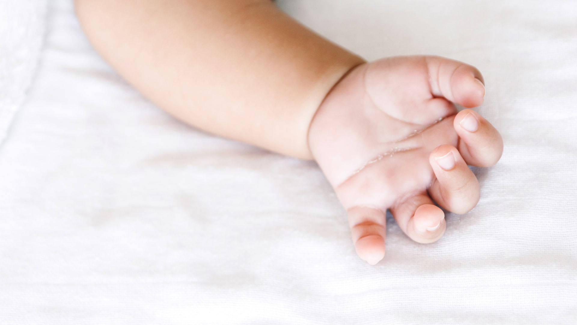 Innocence Cradled: Baby Hand Resting On A White Sheet