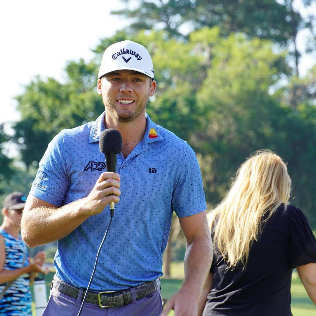 Inspiring Champion; Sam Burns Holding A Microphone Background