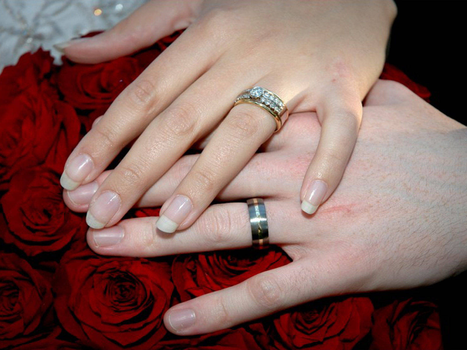 Intimate Holding Hands With Rings On Roses Background