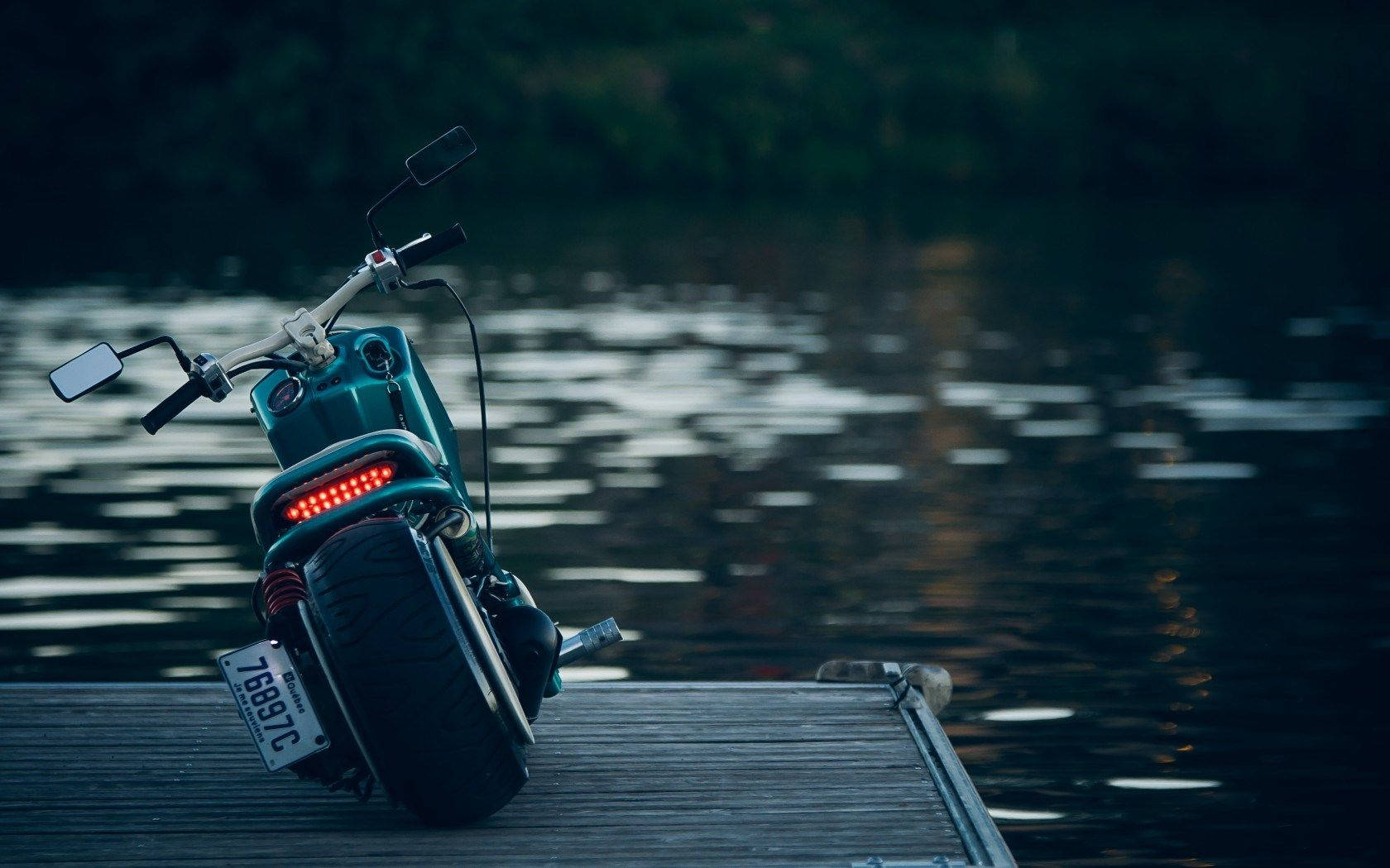 Intrepid Explorer Riding On A Motorcycle Near A Pristine Alpine Lake Background