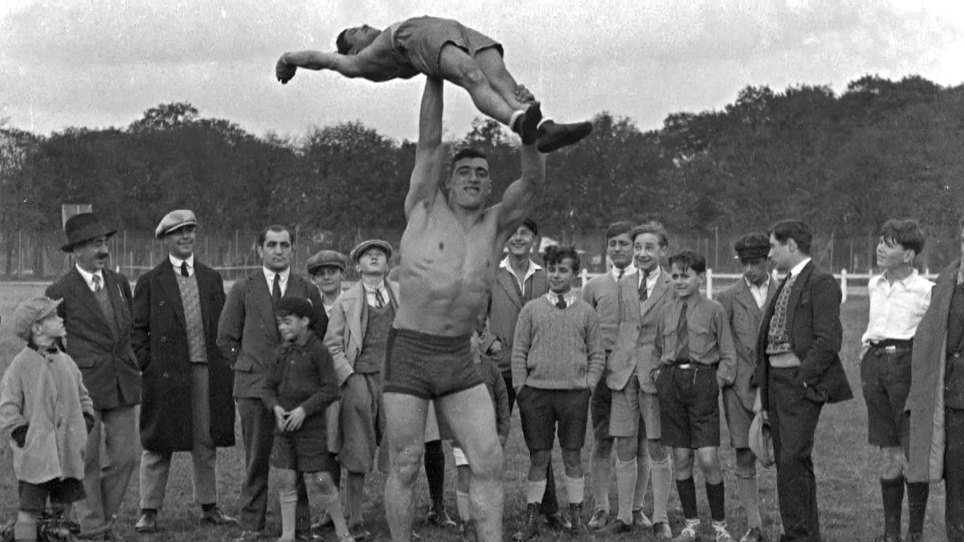 Italian Professional Boxer Primo Carnera Lifting A Man Background
