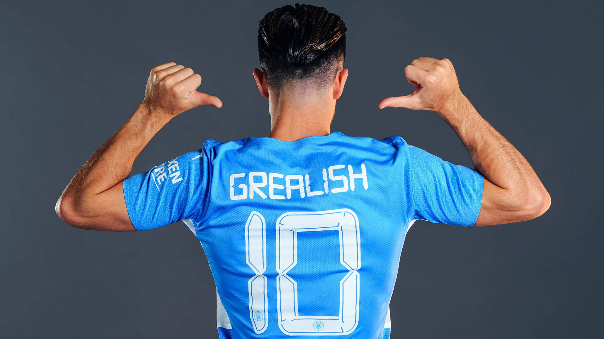 Jack Grealish Pointing At His Name On His Football Jersey Background