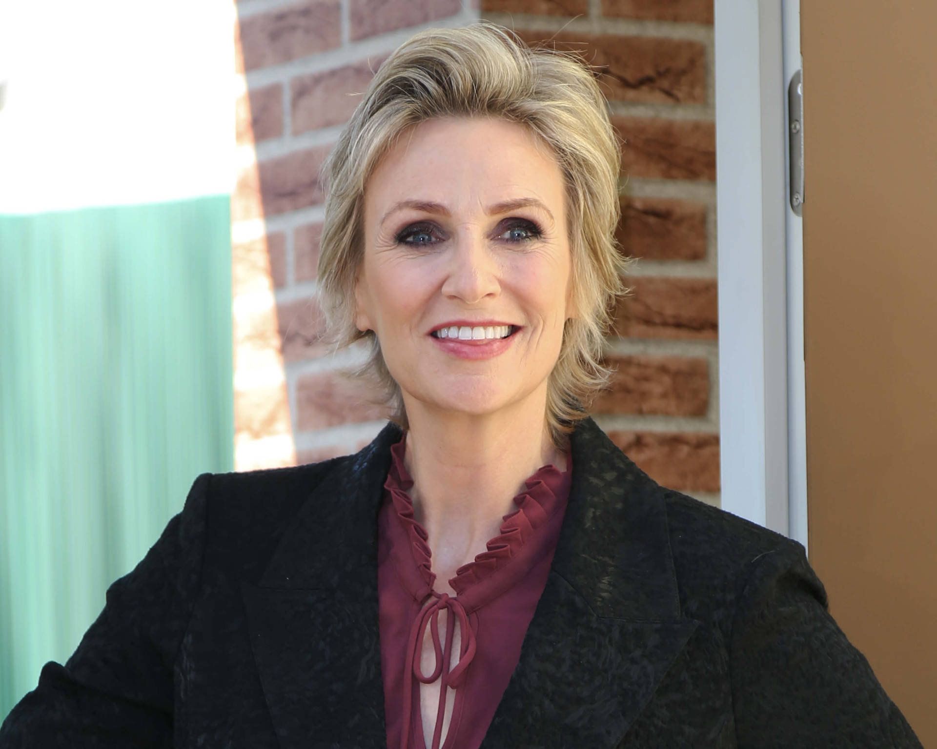 Jane Lynch Actress Purple Shirt And Black Coat Background