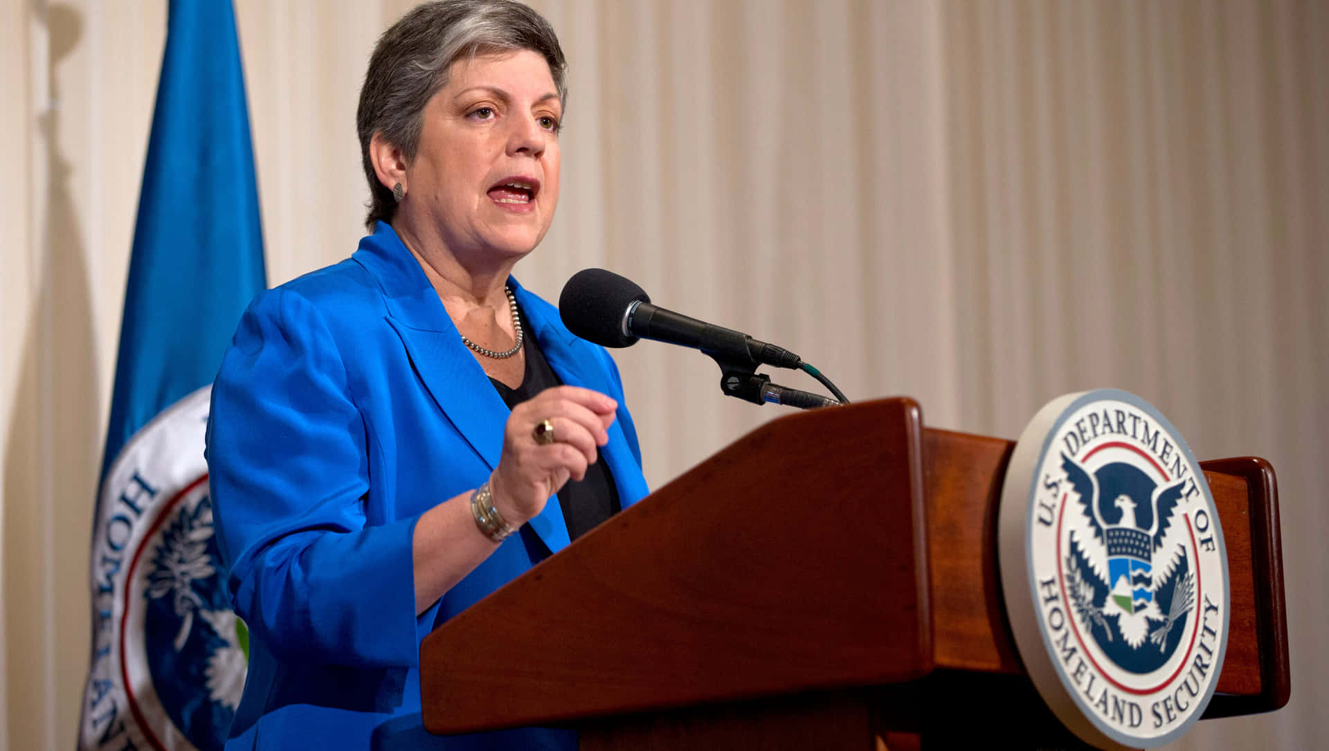 Janet Napolitano Speaking On Podium Background