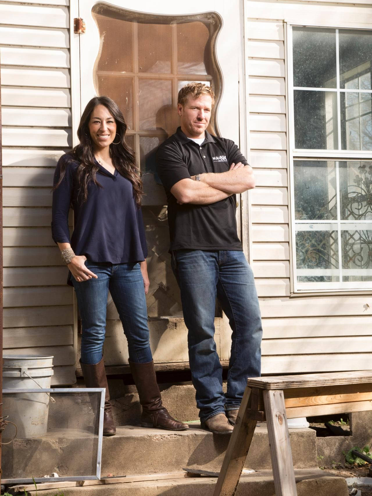 Joanna And Chip Gaines Standing In Front Of Their Iconic Farmhouse Background