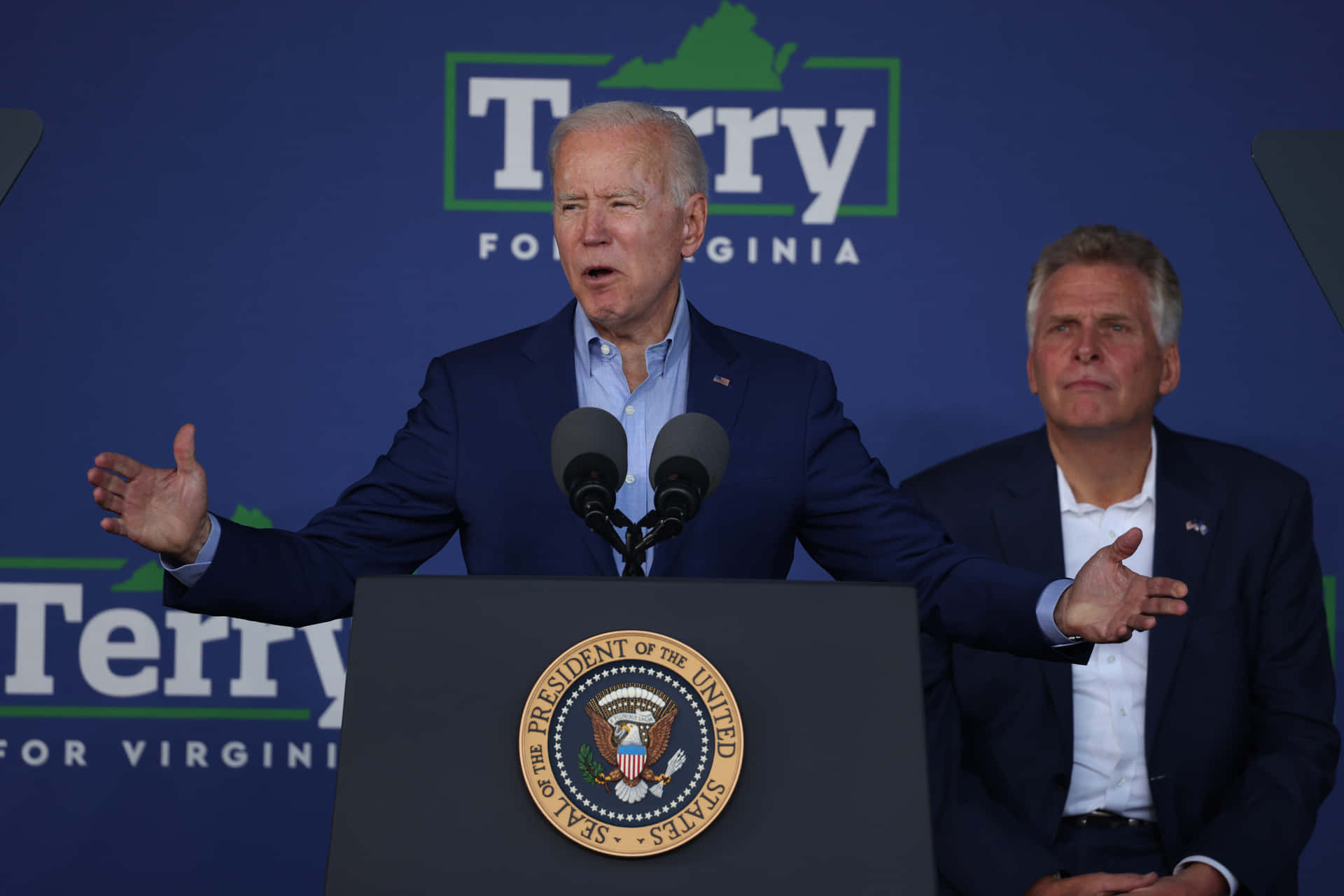 Joe Biden Delivering A Speech With Terry Mcauliffe Behind Him Background