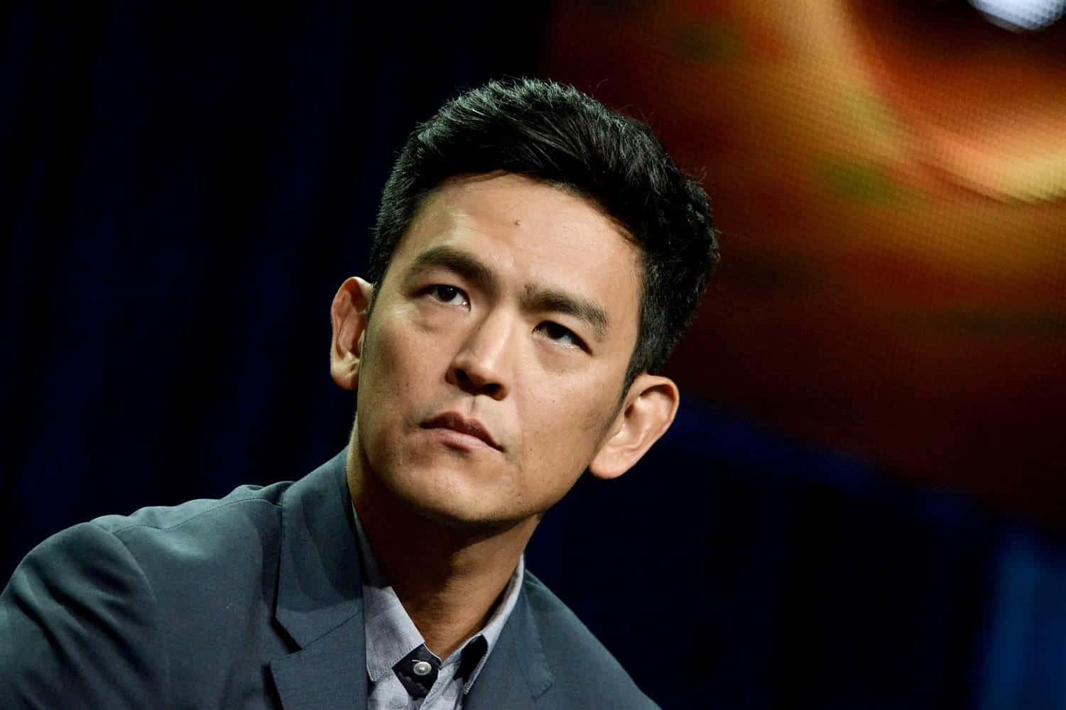 John Cho Smiling In A Stylish Outfit Against A Blue Background Background