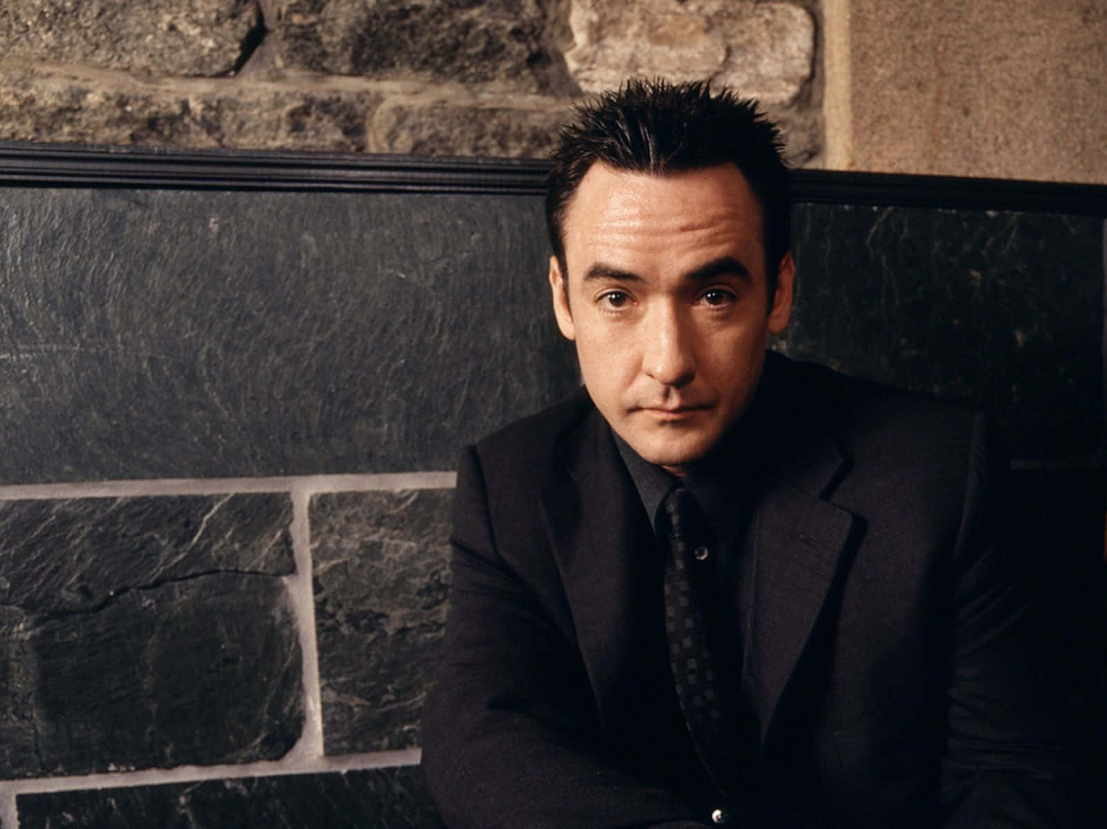John Cusack Posing With A Black Leather Jacket Background