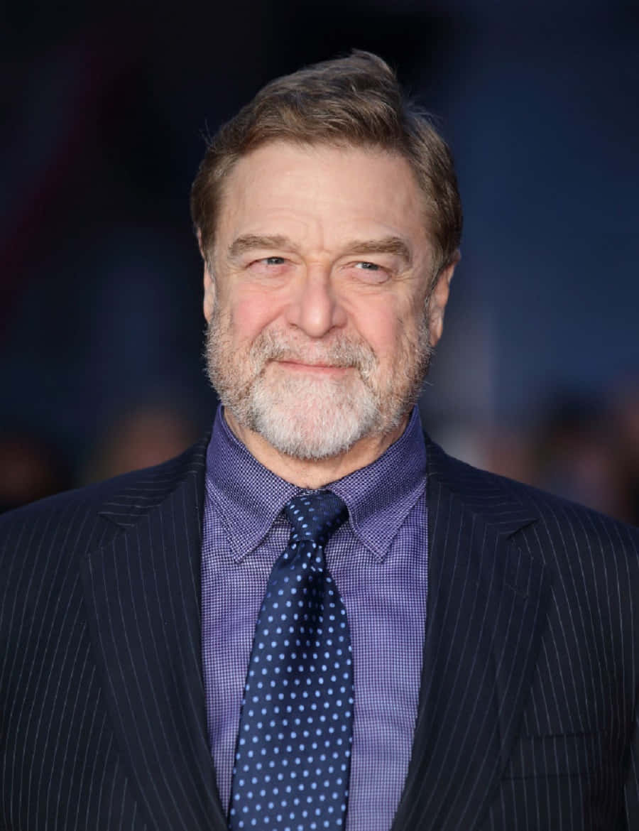 John Goodman Smiling In A Suit Background