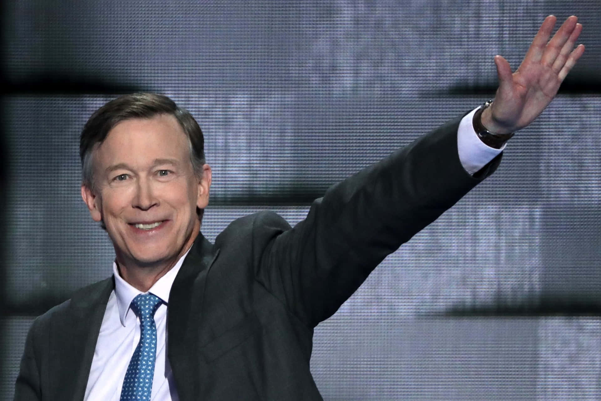 John Hickenlooper Waving With A Gray Background