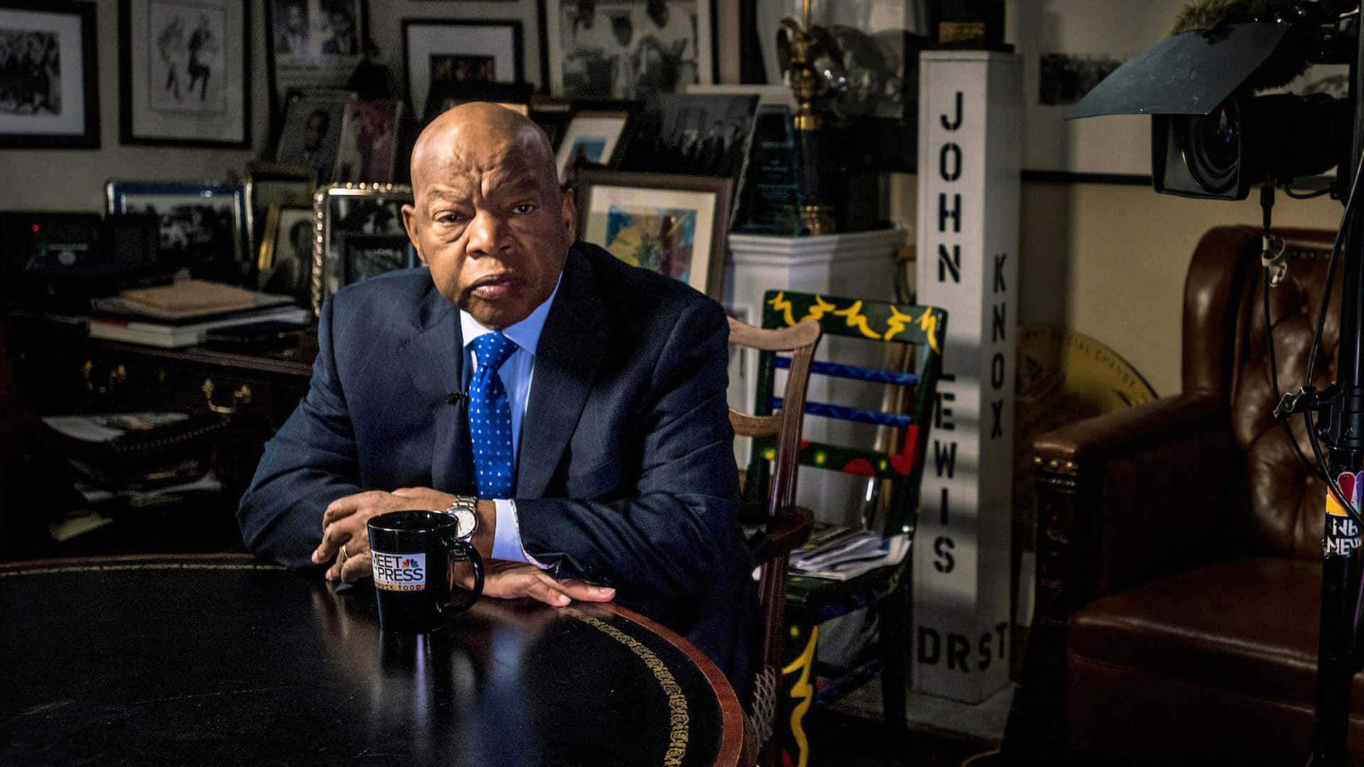 John Lewis Engaged In Deep Thought At A Meeting Table Background