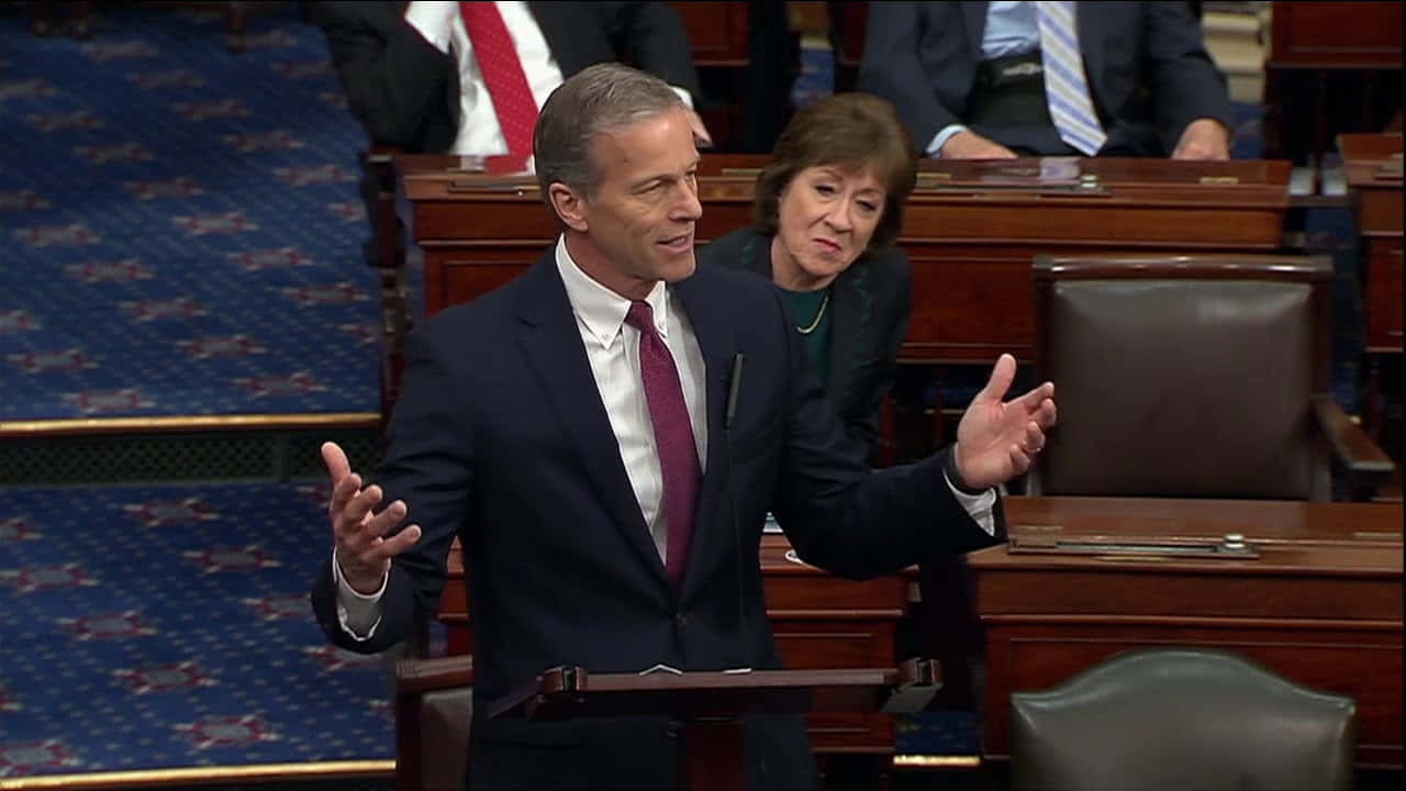 John Thune Shrugging At A Podium Background