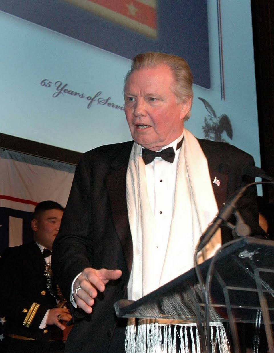 Jon Voight Delivering A Speech On A Podium Background