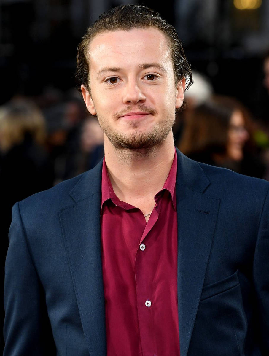 Joseph Quinn Smiling In Red Shirt Background