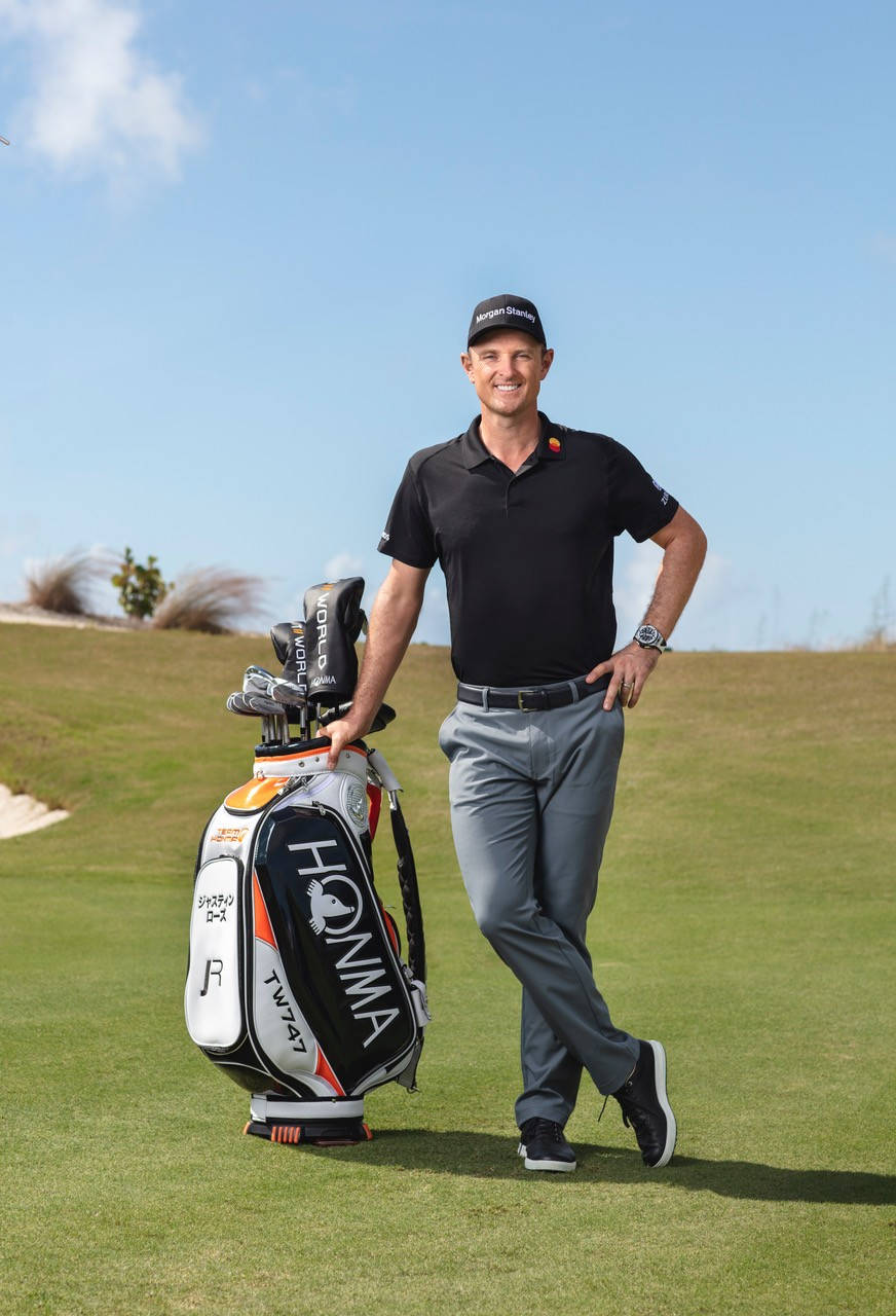 Justin Rose Leaning On A Golfing Bag Background