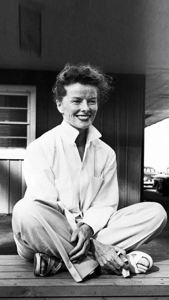 Katharine Hepburn Seated On A Wooden Floor Background