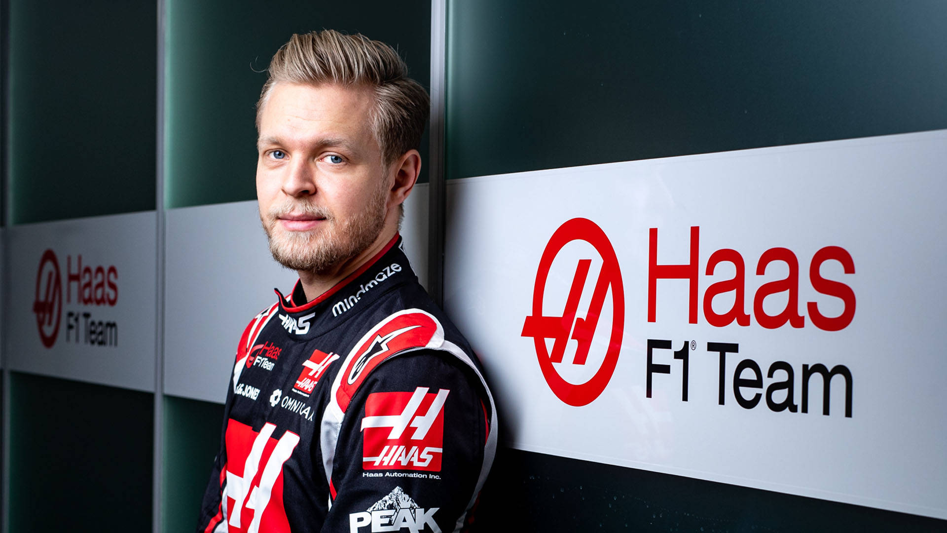 Kevin Magnussen Leaning Casually Against A Wall Background