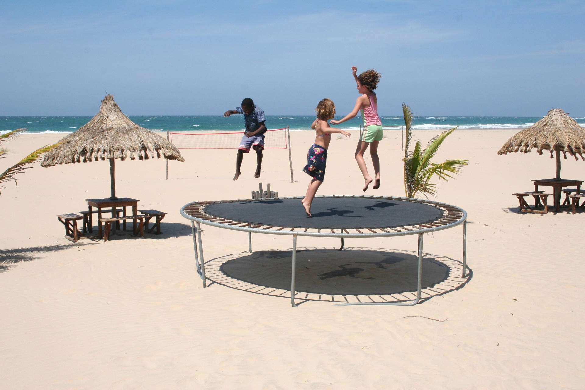 Kids Jumping On A Trampoline Near The Beach Background