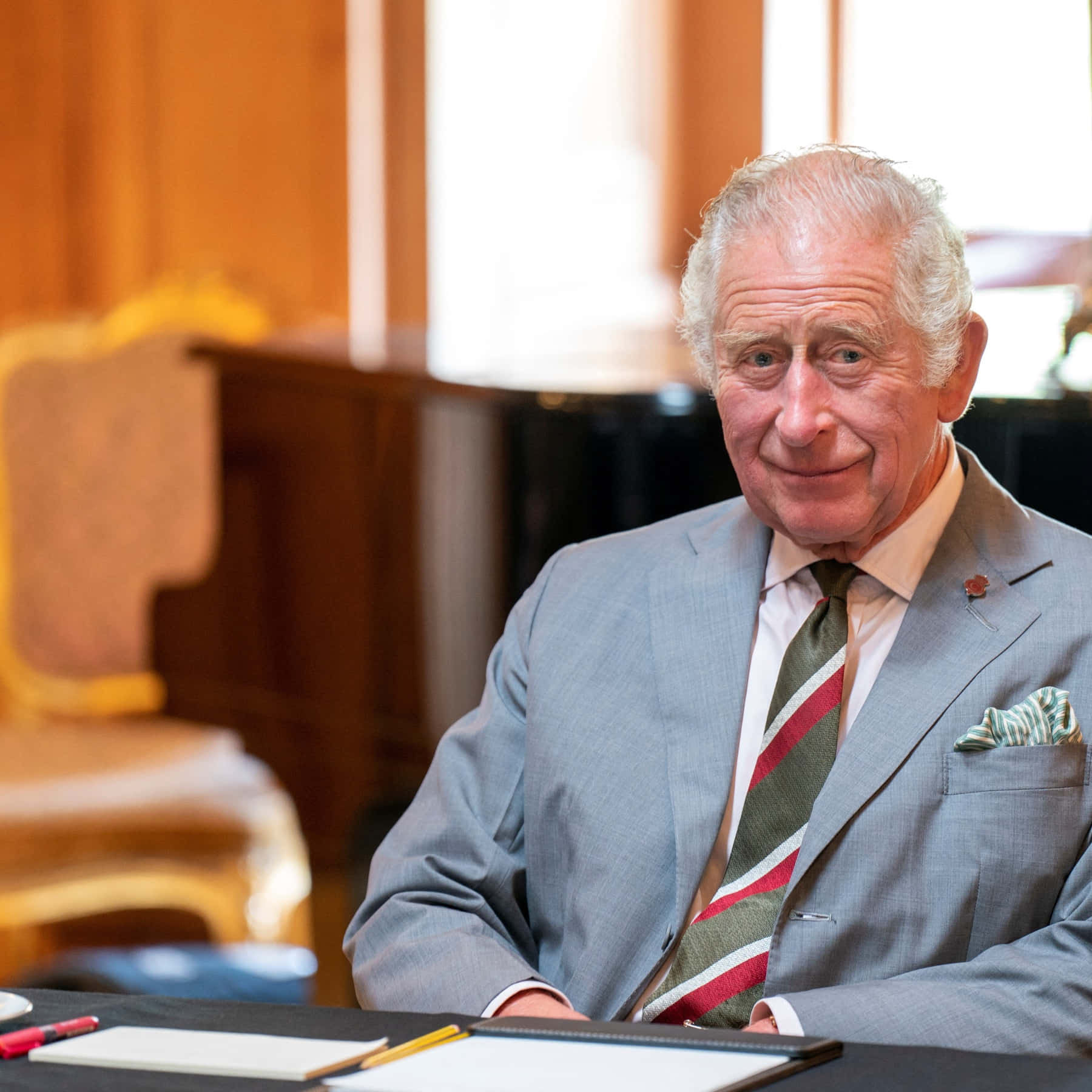 King Charles Iii Smirking Behind Desk Background