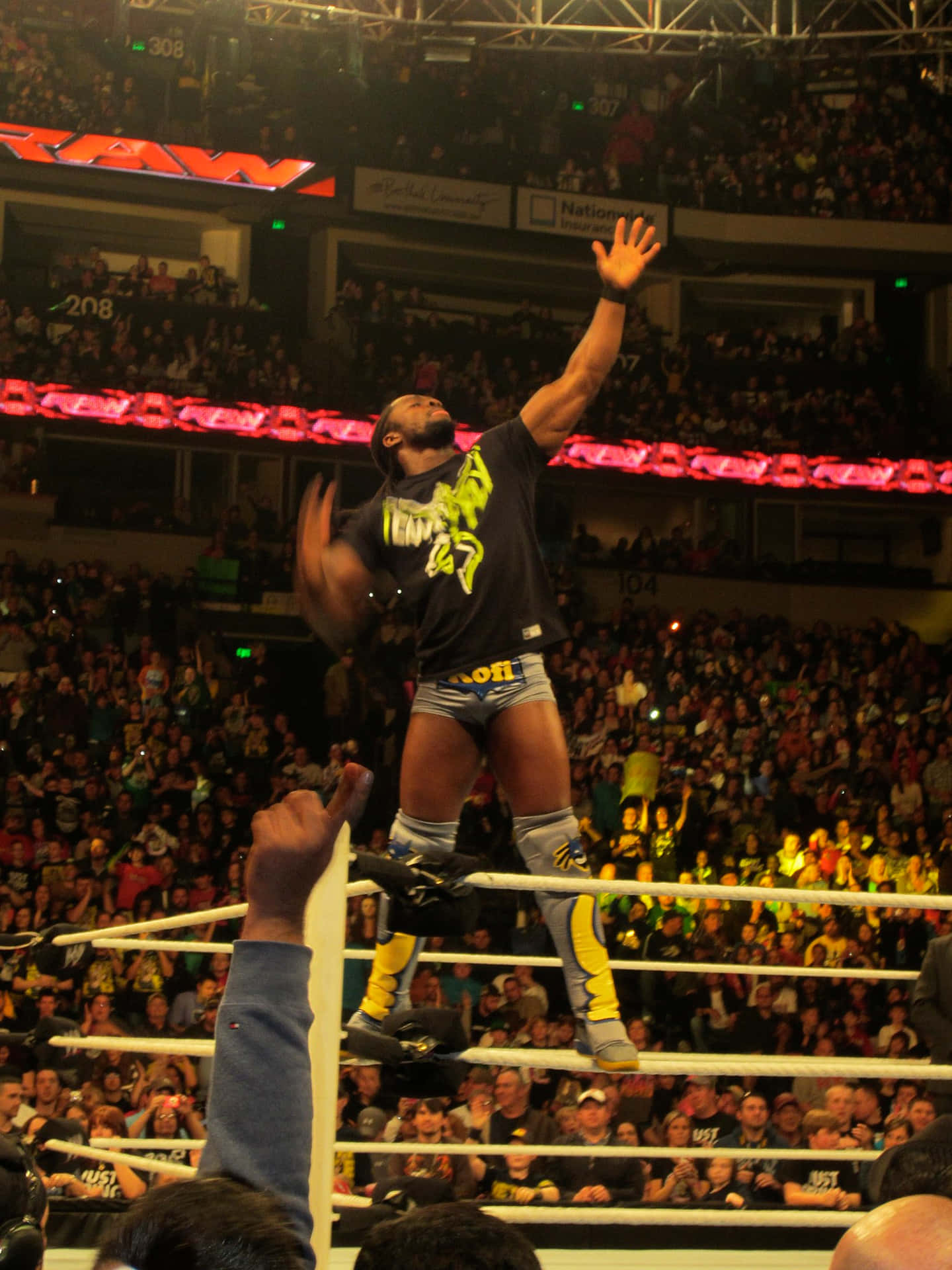 Kofi Kingston Triumphantly Stands On Wrestle Ring Ropes Background