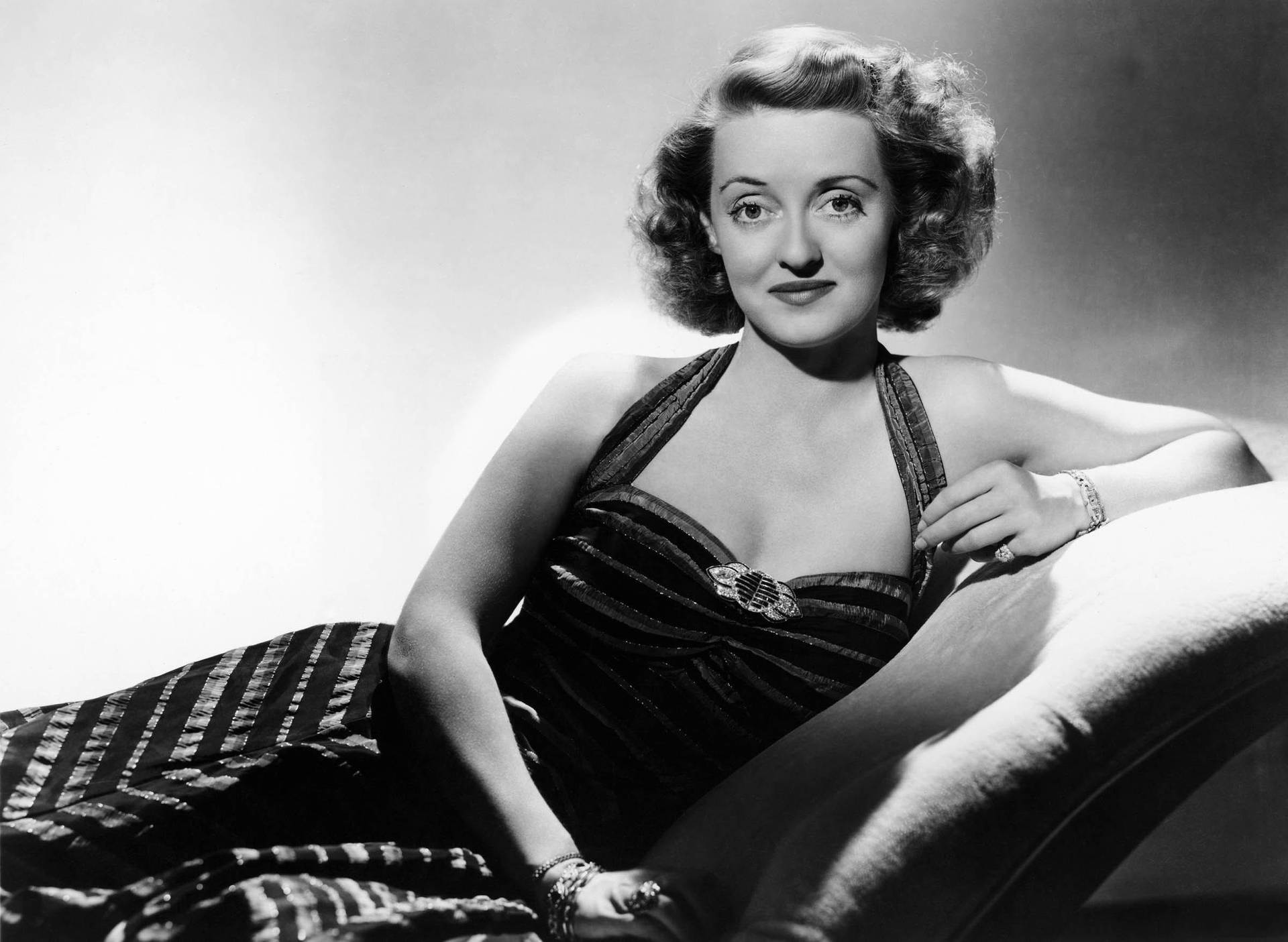 Legendary Bette Davis Relaxing On A Couch Background