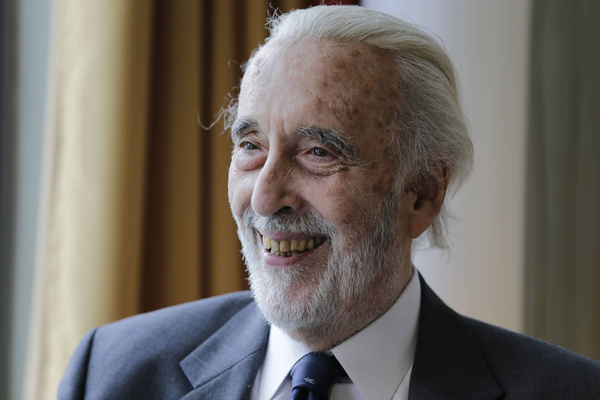 Legendary British Actor Christopher Lee Flaunting A Happy Glance Background