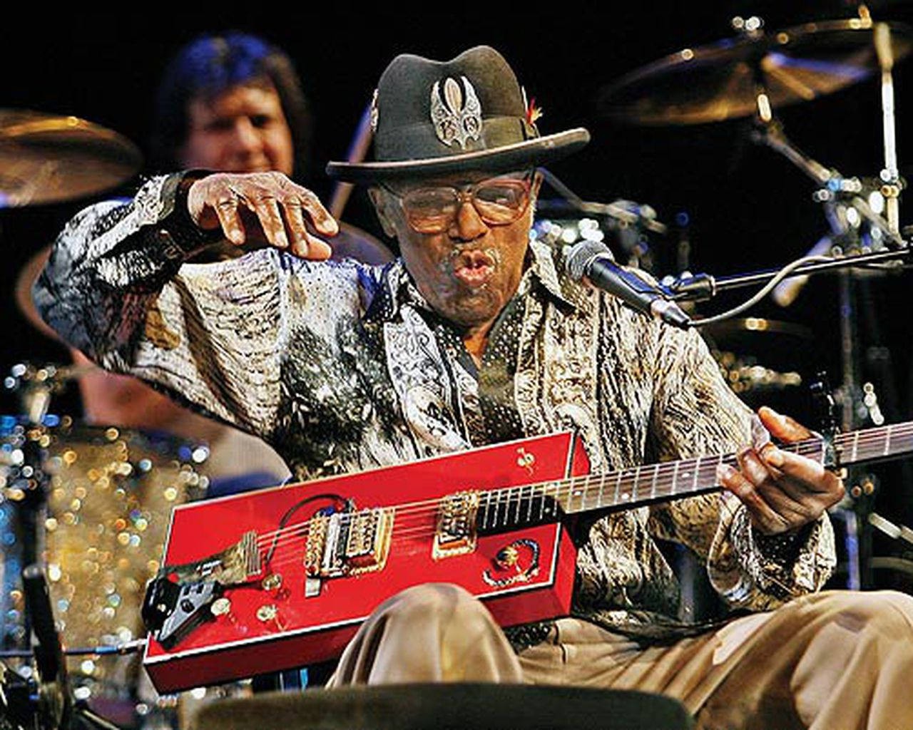 Legendary Musician Bo Diddley Showcasing His Unique Guitar Skills Background