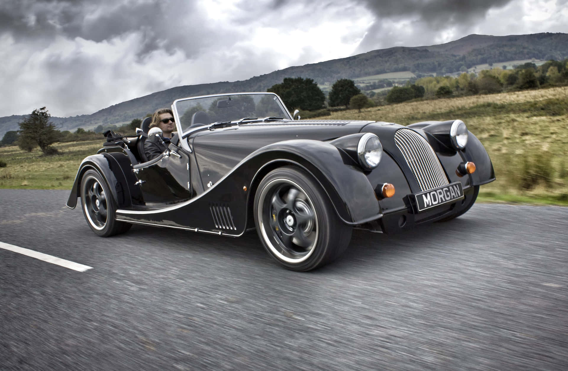 Majestic Morgan Sports Car On A Scenic Road Background