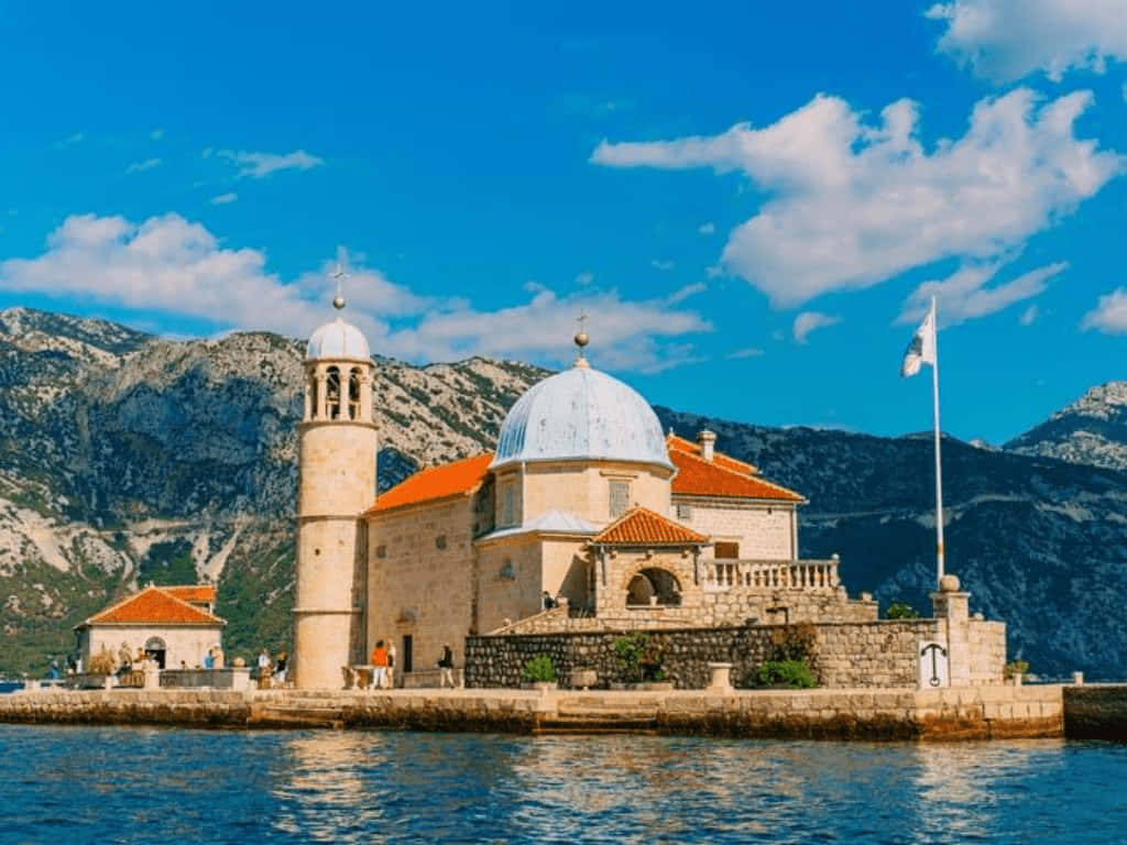 Majestic Our Lady Of The Rocks Church Against A Scenic Mountain Backdrop