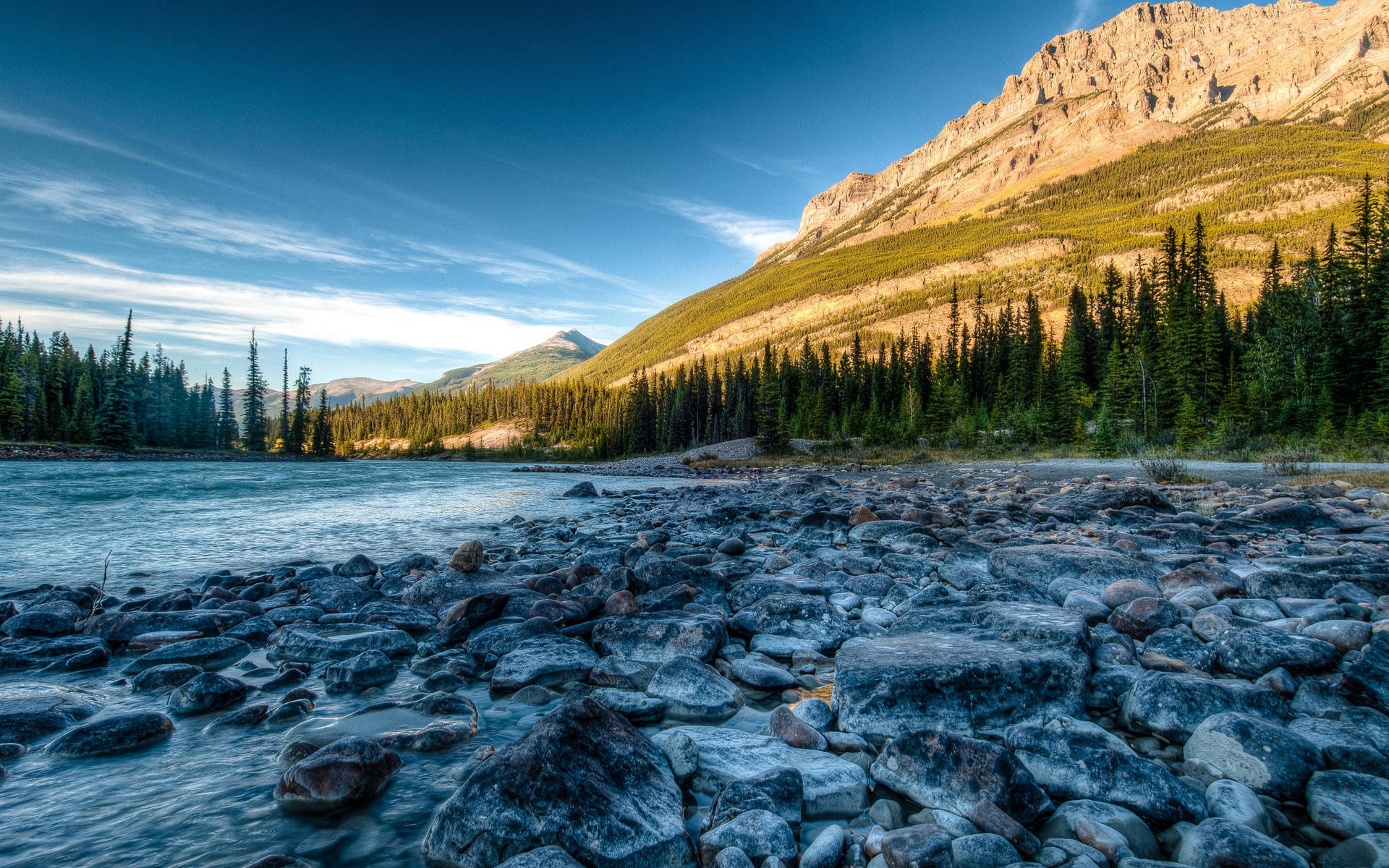 Majestic Rocky Mountain Landscape Featuring A Serene Lake And A Stone Covered Shoreline Background