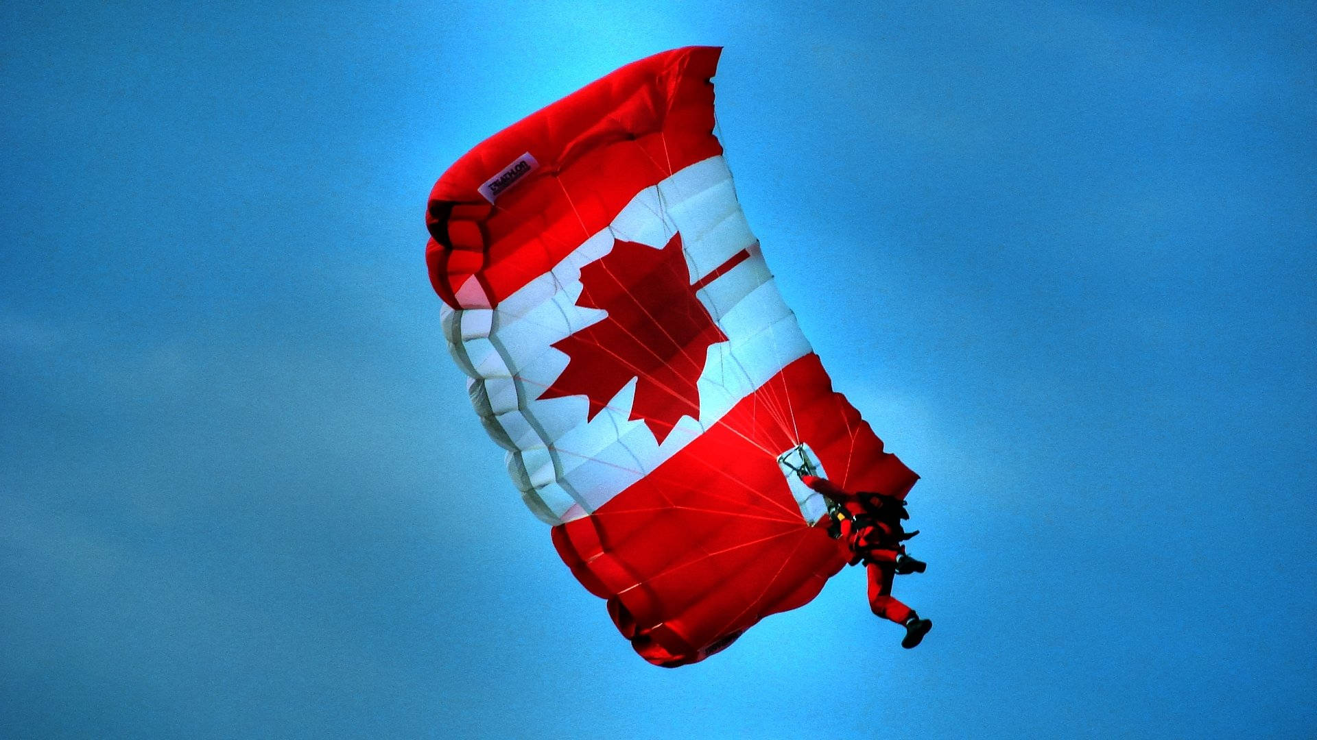 Majestic Shot Of Canada Flag Floating On A Parachute Against The Blue Sky Background