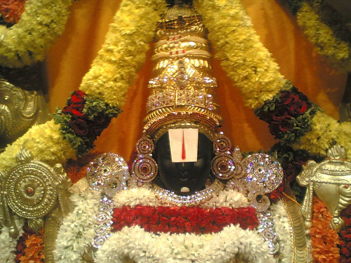 Majestic Tirupati Balaji Statue Adorned With Vibrant Flower Garlands Background