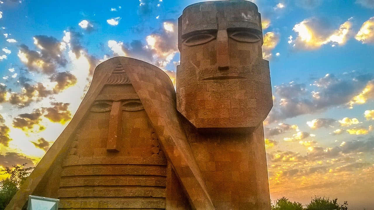 Majestic View Of We Are Our Mountains Monument Against A Vibrant Sunset Background