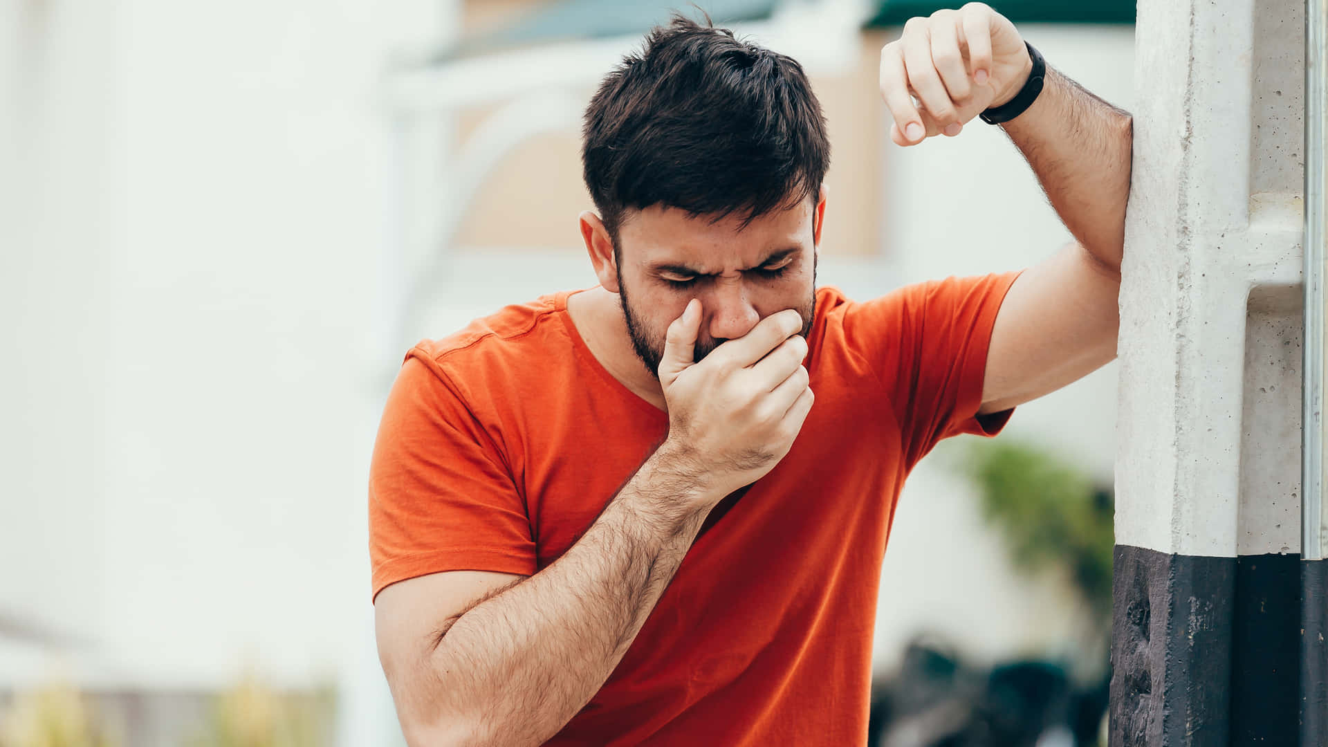 Man Feeling Nauseous In Orange Shirt Against A Natural Backdrop