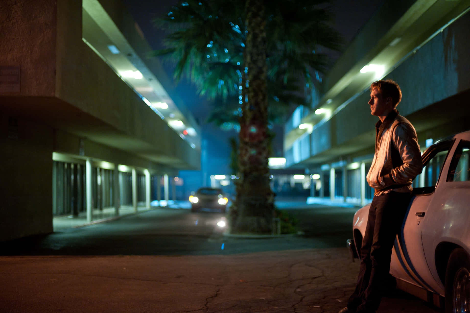 Man Leaningon Carin Parking Lotat Night Background