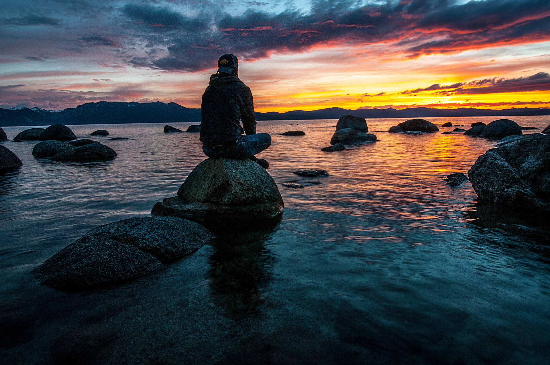 Man Sitting Alone On Rocky Beach Background